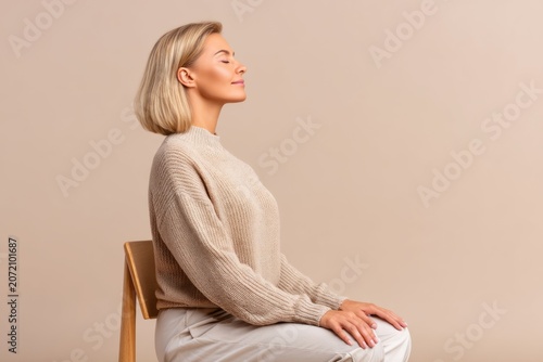 Woman sitting on chair with eyes closed practicing deep breathing exercise. Relaxation technique for pelvic floor health and wellness. Calm adult female resting in meditation pose.