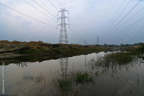 High voltage Electrical power lines supplying electricity to Purulia, West Bengal, India. Sky background and waterbody foreground.