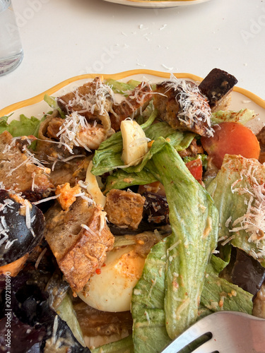 Fresh mixed salad bowl with romaine lettuce, grilled chicken, avocado, croutons, tomatoes, cheese, nuts, and creamy dressing on white table, healthy lunch meal served from above