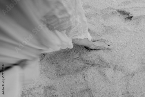 Bare foot stepping through soft beach sand with flowing fabric and gentle blur in monochrome close up, creating serene abstract texture, coastal mood, and quiet sense of movement