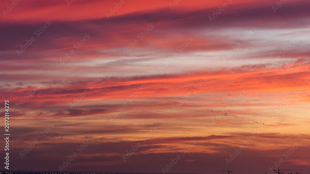 Fototapeta premium Vibrant sunset sky with shades of orange, pink, and purple clouds over a distant horizon, illuminated by the fading light of day