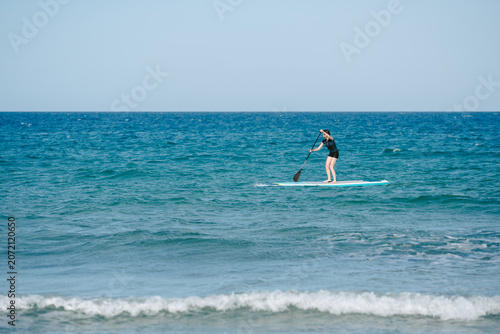 Woman paddleboarding on blue ocean water during summer vacation