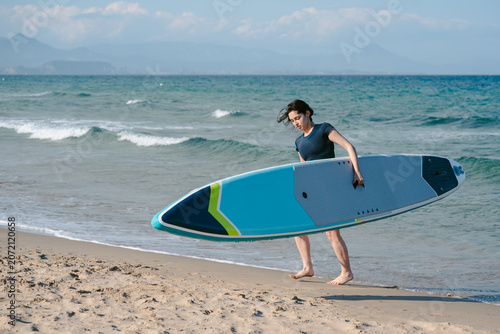 Woman carrying paddleboard walking on beach shore