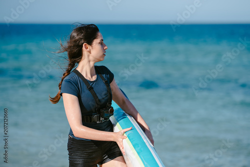 Woman carrying paddleboard by ocean with action camera