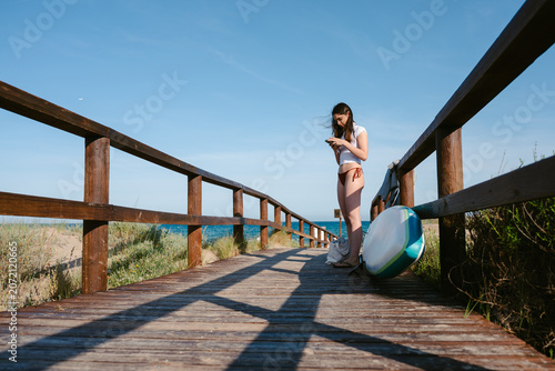 Woman on boardwalk using smartphone before paddleboarding