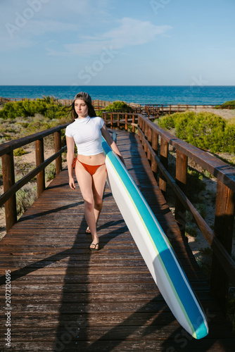Woman carrying paddleboard walking wooden boardwalk beach