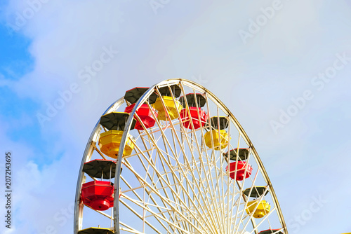 Ferris wheel with red, yellow and black cabins against a dramatic cloudy sky at an outdoor summer fair attraction