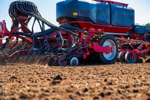 Close up air seeder drill deposits seed rows in tilled soil under bright daylight. Dual seed and fertilizer tanks and manifold identify modern no till practice.