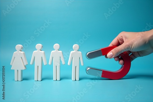 Close-up of a hand using a horseshoe magnet to attract white human figures against a blue backdrop, symbolizing attraction, magnetism, and staffing strategies.