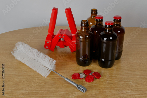 Grupo de botellas de cervezas artesanal, chapadora, limpiador de botellas y chapas rojas sobre mesa de madera