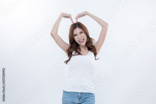 Woman makes heart shape with hands while smiling in front of a white background