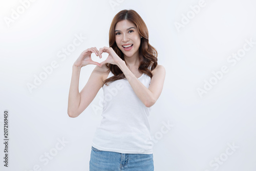 Woman makes heart shape with hands while smiling in front of a white background