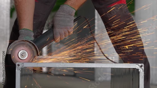 Close-up of a worker in gloves cutting metal with an angle grinder tool in a workshop