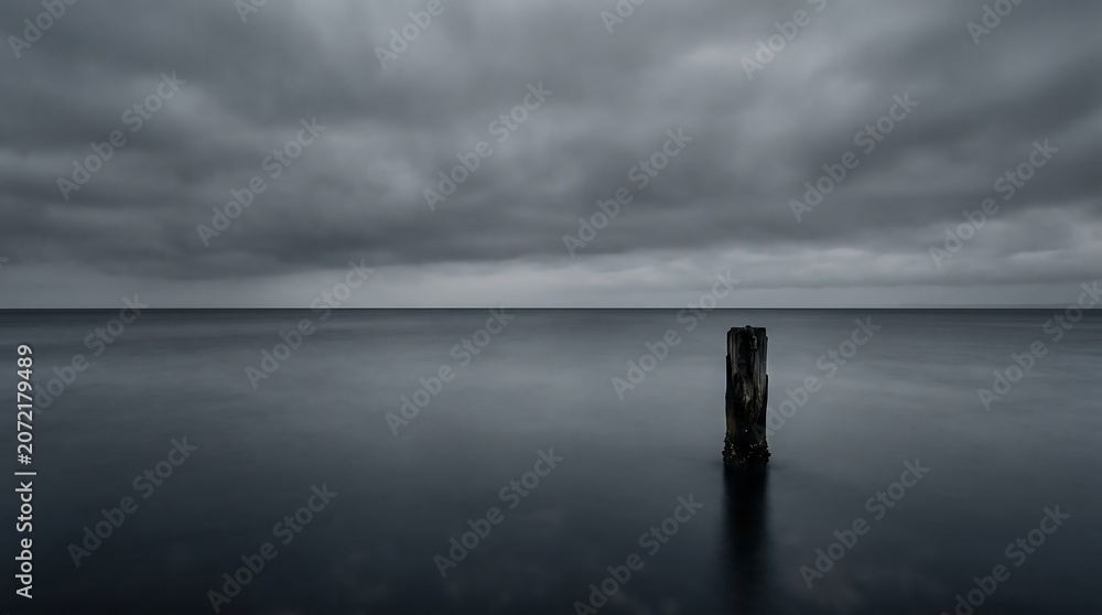 Fototapeta premium Dark ocean water with single post under cloudy sky