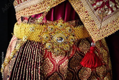 Close up of a luxury Thai traditional wedding dress with elegant golden embroidery, exquisite fabric details, and an ornate antique gold belt. Cultural heritage fashion.