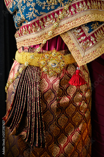 Close up of a luxury Thai traditional wedding dress with elegant golden embroidery, exquisite fabric details, and an ornate antique gold belt. Cultural heritage fashion.