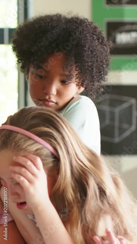 Vertical video: Reacting to peer shielding face in class, child behind leaning, soothing, pale top