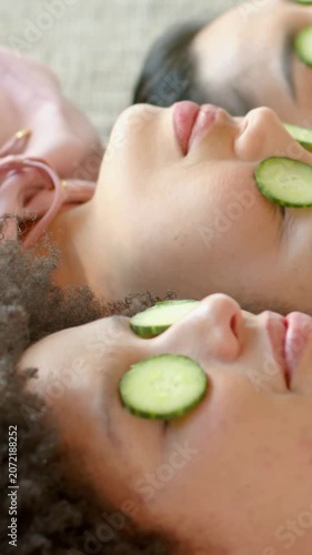 Vertical video: Lying 3 women relaxing on mat at spa for skincare, with cucumber slices pink strap