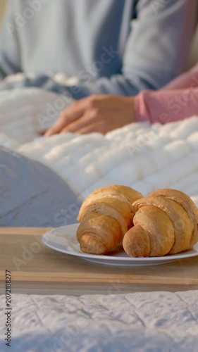 Vertical video: Starting with still tray, pink person moving hands across quilt at bed, croissants