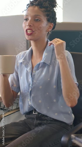 Vertical video: Chat starting, woman in blue top gesturing and explaining work at cubicle with mug