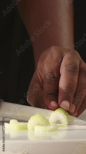 Vertical video: Slicing hand steadying pale green veg on board, cutting uniform slices with knife