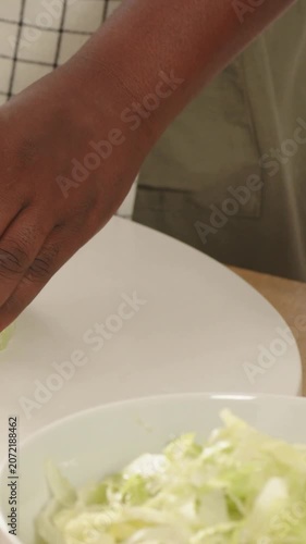 Vertical video: Reaching hand tearing cabbage in kitchen, adding pieces into bowl for salad, apron