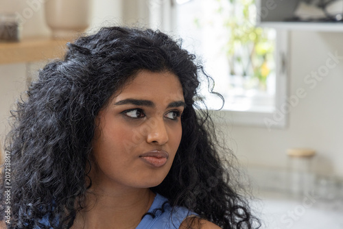 Obraz na plátně Indian woman sitting in home kitchen, wearing sleeveless blue top, gazing toward