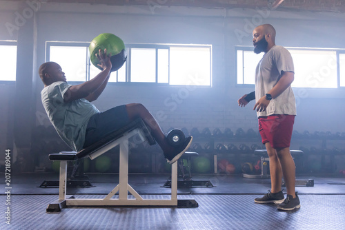 Obraz na plátně African American male trainer coaching client doing green med ball twist on incl