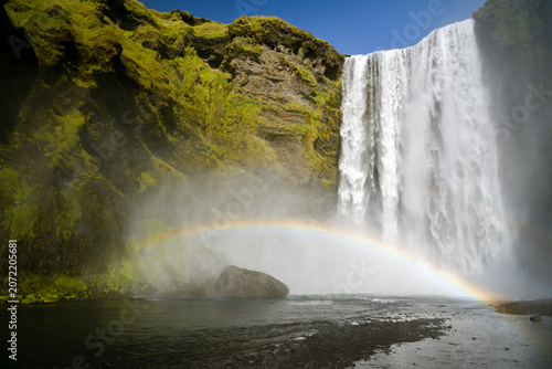 Waterfall with a full rainbow over a mossy cliff