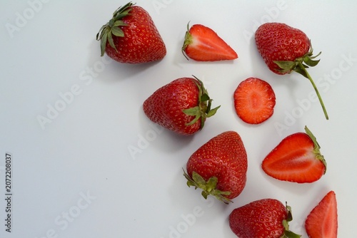Minimalist flat lay of fresh strawberries and sliced strawberry pieces on white background. Clean food composition with advertising copy space.