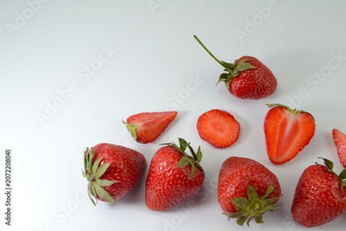 Fresh ripe strawberries and strawberry slices arranged in minimalist composition on white background with large copy space. Healthy summer fruit concept.