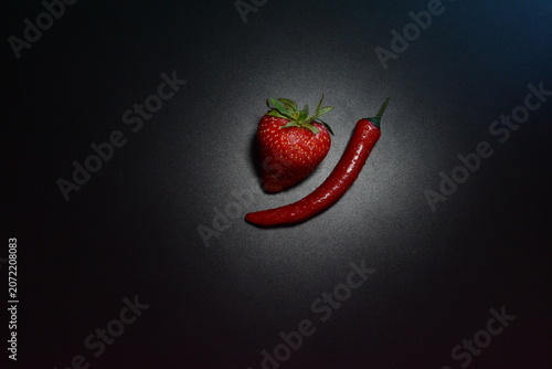 Creative contrast composition with fresh strawberry and red chili pepper on dark black background. Sweet and spicy food concept with copy space.
