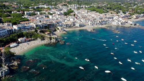 Aerial view of Calella de Palafrugell, a charming Costa Brava fishing village overlooking Canadell Beach, with whitewashed houses, turquoise waters and traditional Mediterranean character. 