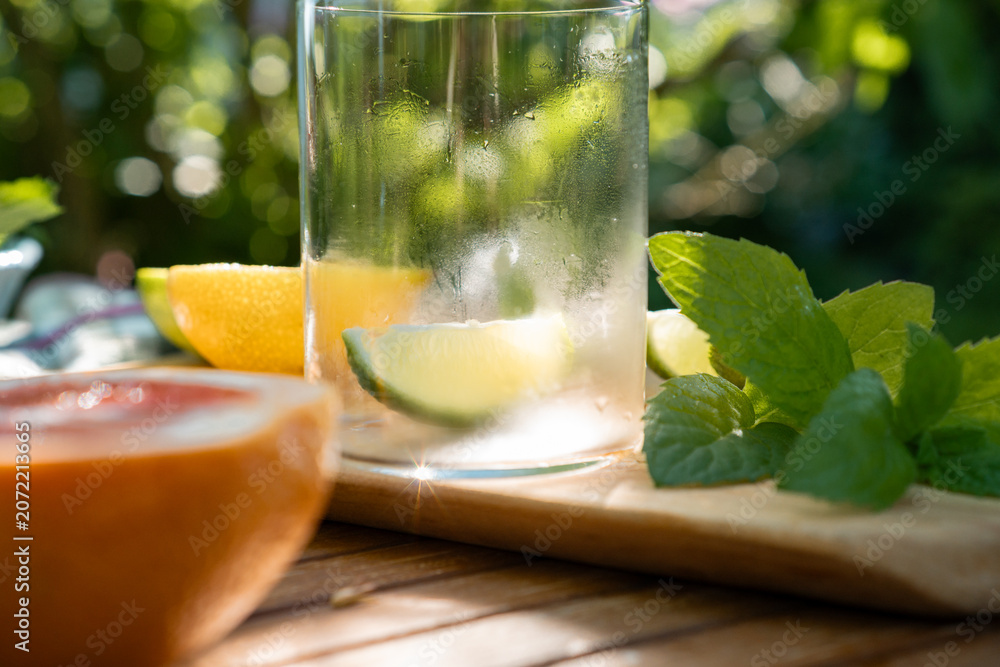 Fototapeta premium Close-up of a fresh lime slice in a glass with mint and sliced citrus fruits prepared on a wooden board outdoors