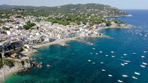 Aerial view of Calella de Palafrugell, a charming Costa Brava fishing village overlooking Canadell Beach, with whitewashed houses, turquoise waters and traditional Mediterranean character. 