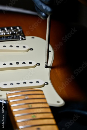 Vászonkép Vertical macro shot of a luthier servicing potentiometers and electronics on a sunburst stratocaster body under a lamp