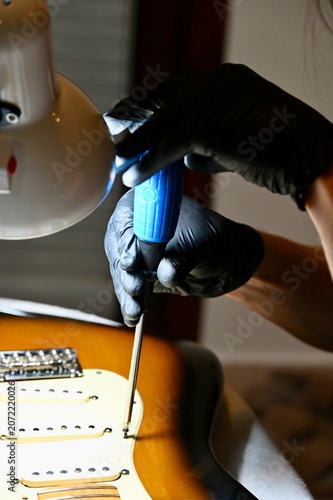 Fényképezés Vertical macro shot of a luthier servicing potentiometers and electronics on a sunburst stratocaster body under a lamp