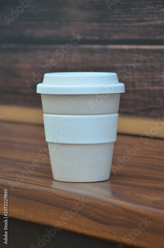 White-beije reusable coffee cup from eco -friendly bamboo material standing isolated on wooden table surface.