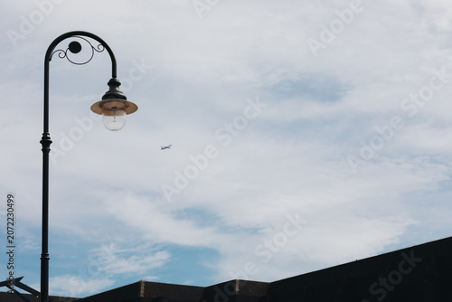 Vintage street lamp against cloudy sky with airplane and urban rooftop