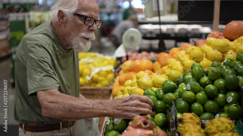 Elderly man enjoys shopping for fresh fruits and vegetables in a grocery store while picking items from the display