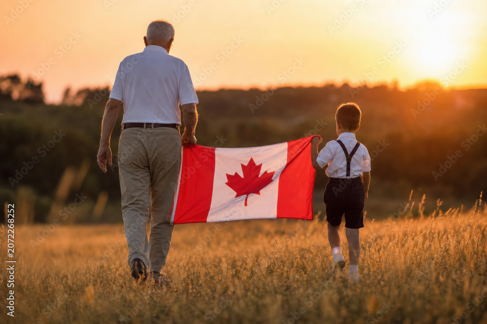 Fototapeta premium Attractive old senior man and grahdson holding Canadian Flag. National holiday. Grandpa retiree. Retirement parent