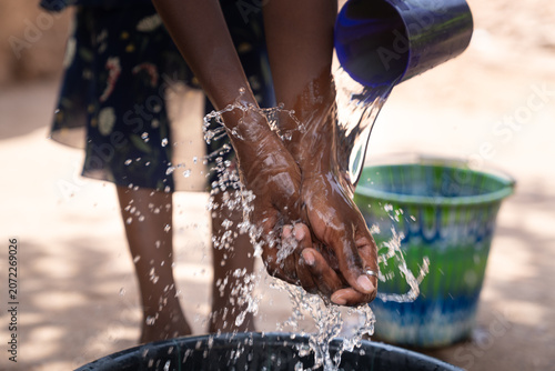 African young girl rinses her hands under a stream of clean water, the splash of the pouring bowl marking the final step before she returns to the meal with the rest of her family.