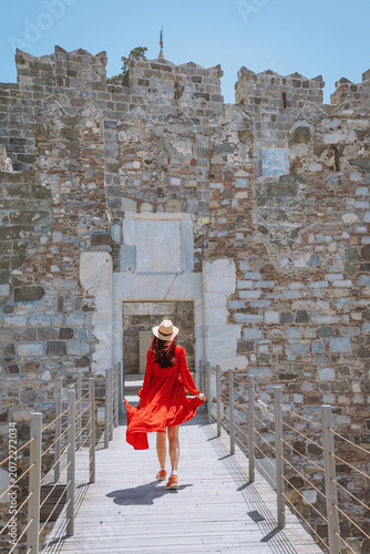 Photos Young woman in a flowing red dress and hat walking towards the ancient entrance