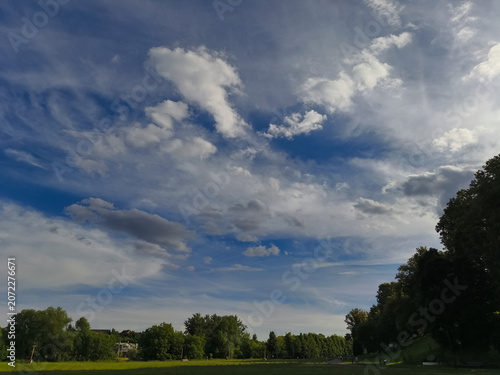 Green field and blue sky with beautiful fluffy clouds in sun summer day. Natural nature panorama cloudscape bright background