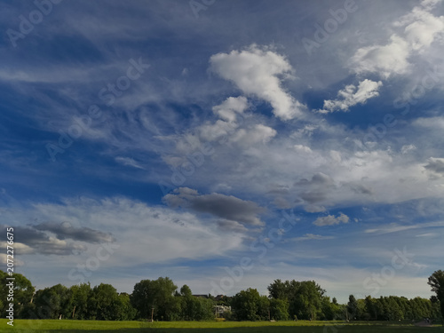 Green field and blue sky with beautiful fluffy clouds in sun summer day. Natural nature panorama cloudscape bright background