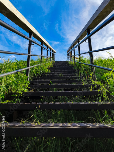 Metal texture stairs ascend a grass hill under to beautiful blue clear sky with warm sun. Nature concept way raise to up, success, elevation, freedom achievement with top ambition. Summer day