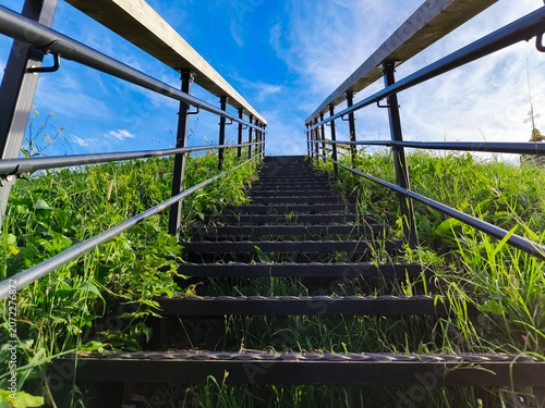 Metal texture stairs ascend a grass hill under to beautiful blue clear sky with warm sun. Nature concept way raise to up, success, elevation, freedom achievement with top ambition. Summer day