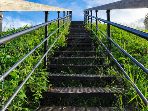 Metal texture stairs ascend a grass hill under to beautiful blue clear sky with warm sun. Nature concept way raise to up, success, elevation, freedom achievement with top ambition. Summer day