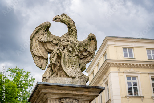 Stone eagle sculpture in Warsaw square on ornate pedestal, historic building, overcast spring sky