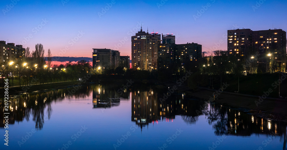 Fototapeta premium City skyline reflecting in calm lake water at dusk with vibrant blue and pink twilight sky
